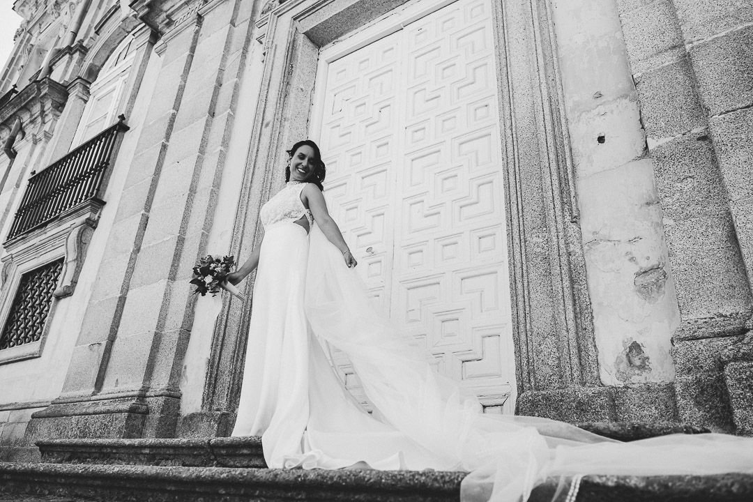 Noelia sonríe con su ramo ante una puerta del palacio, en blanco y negro.