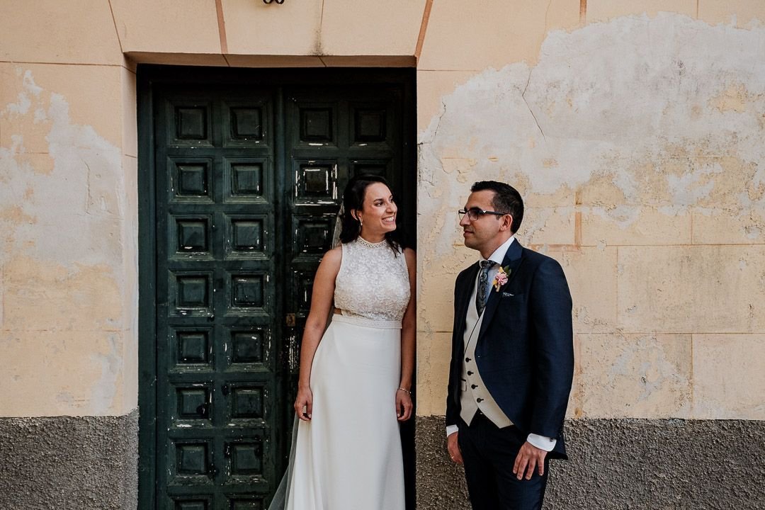 Noelia y Carlos sonríen ante una puerta verde de madera.