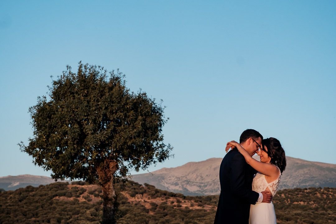 Noelia y Carlos abrazados junto a un árbol, con las montañas al fondo.