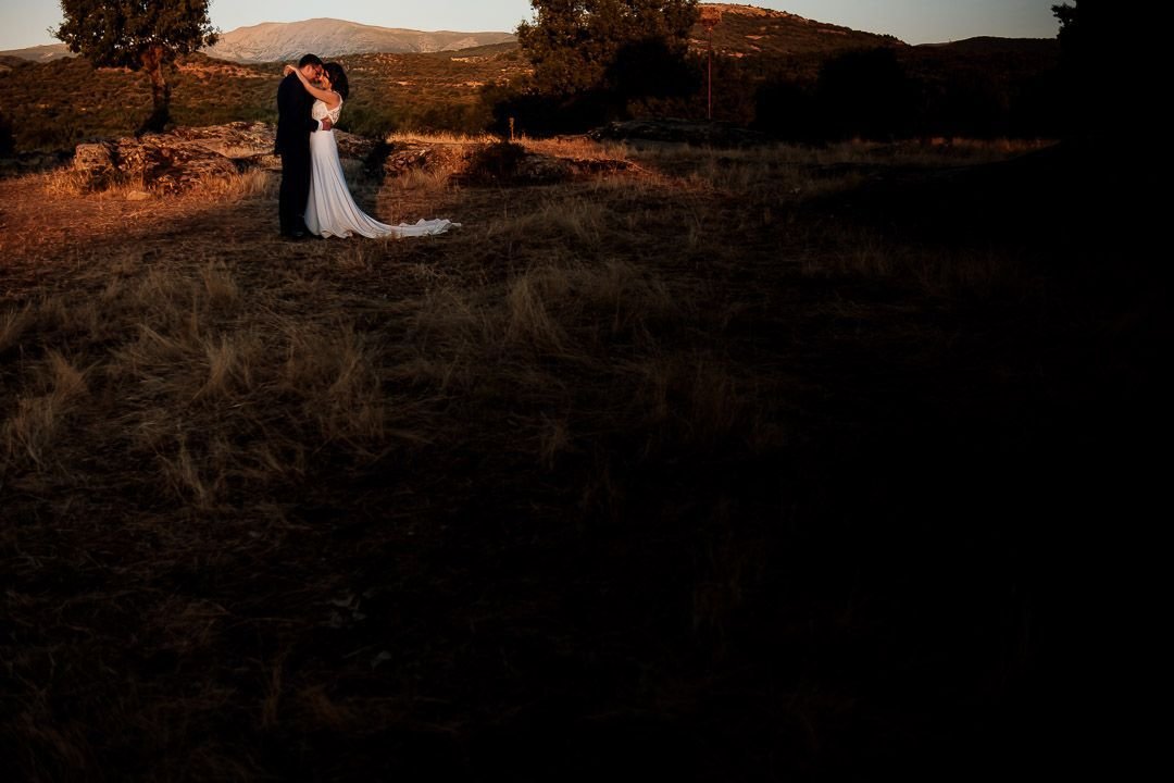 Plano abierto de los novios abrazados en el paisaje al final de la tarde.