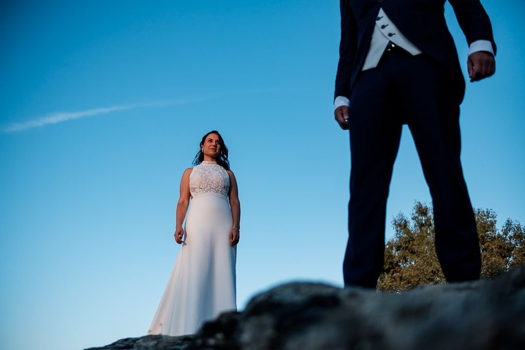 Noelia sobre unas rocas y Carlos en primer plano, bajo el cielo azul.