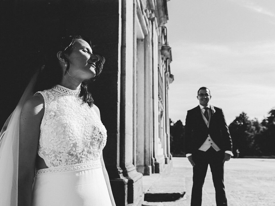Retrato en blanco y negro de Noelia junto a la fachada, con Carlos al fondo.