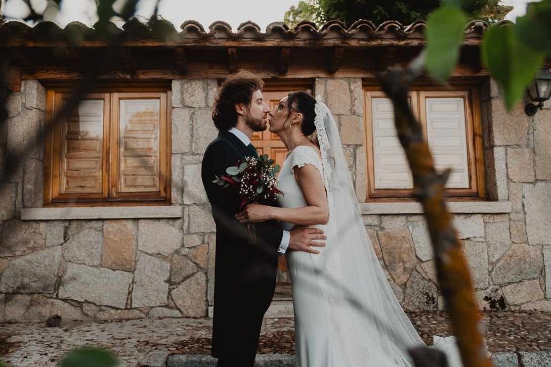 Natalia y David se besan ante una fachada de piedra con ventanas de madera.