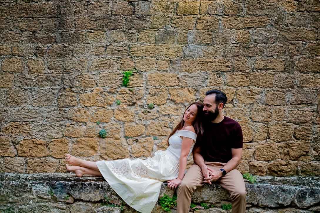 Lara, descalza, y Javi sentados juntos junto a un muro de piedra.