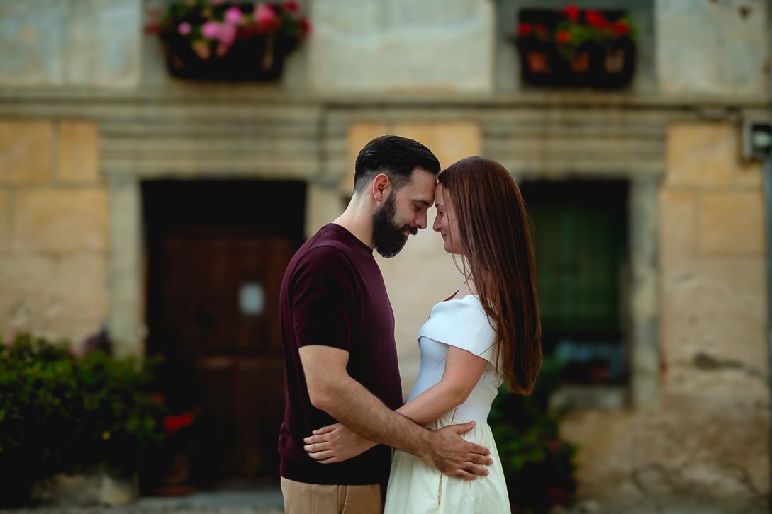 Lara y Javi unen sus frentes ante una fachada con macetas en Pedraza.