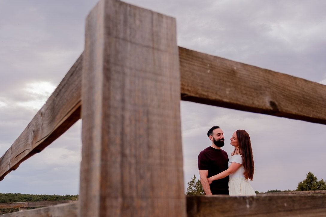 La pareja abrazada, enmarcada por una valla de madera bajo el cielo nublado.