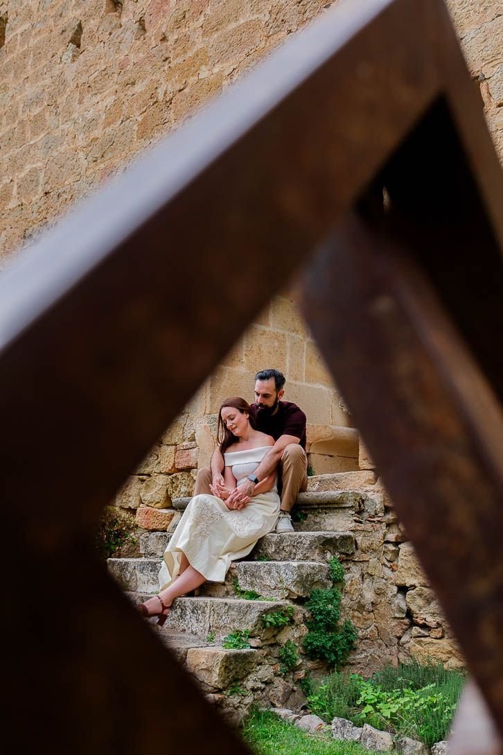 La pareja sentada en unas escaleras de piedra, vista a través de una barandilla.