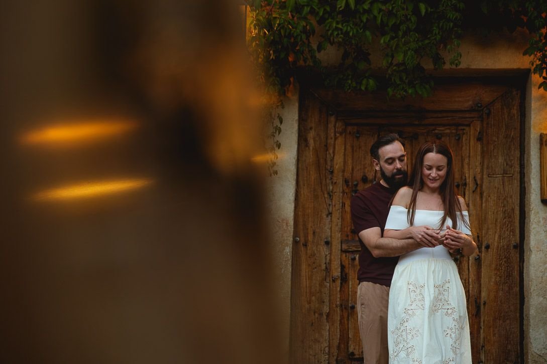 Lara y Javi se abrazan ante una puerta de madera, con reflejos cálidos en primer plano.