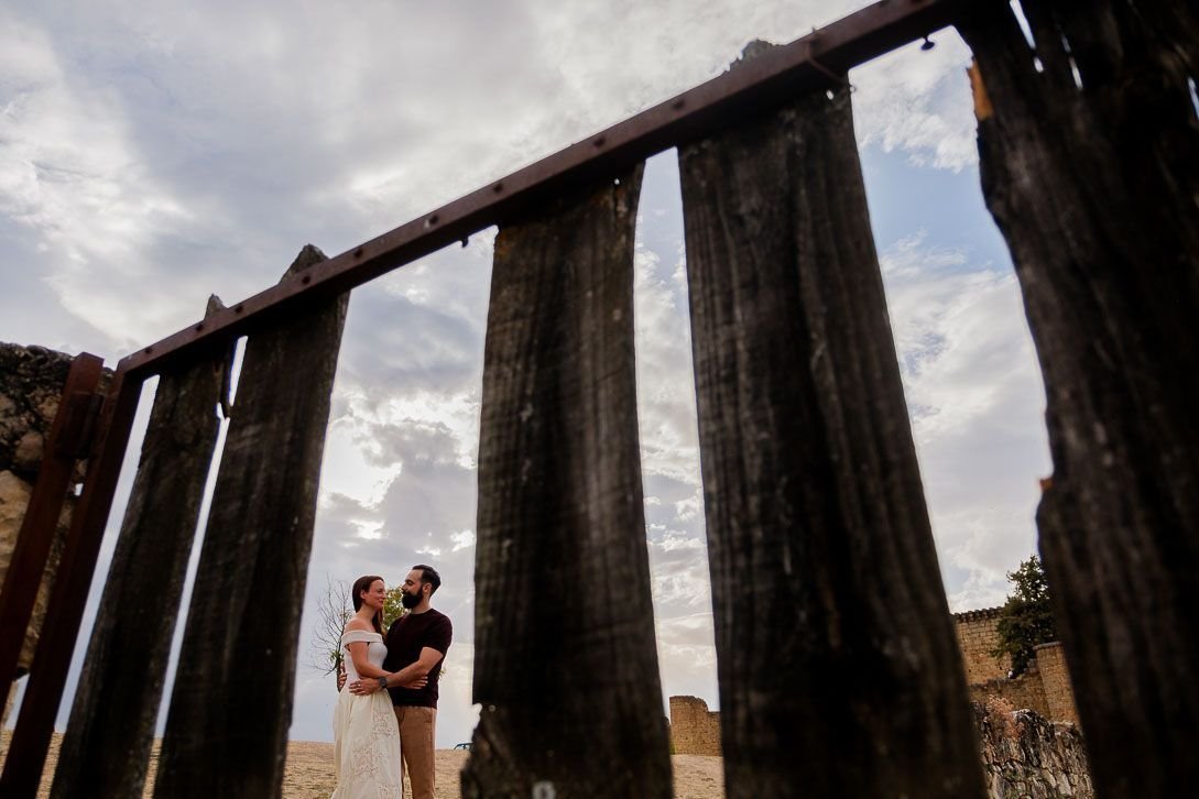 Lara y Javi abrazados, vistos entre las tablas de una valla de madera.