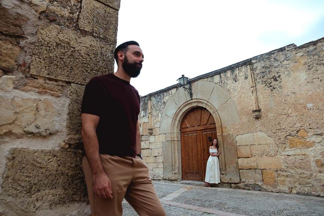 Javi apoyado en una esquina y Lara junto a una puerta con arco al fondo.