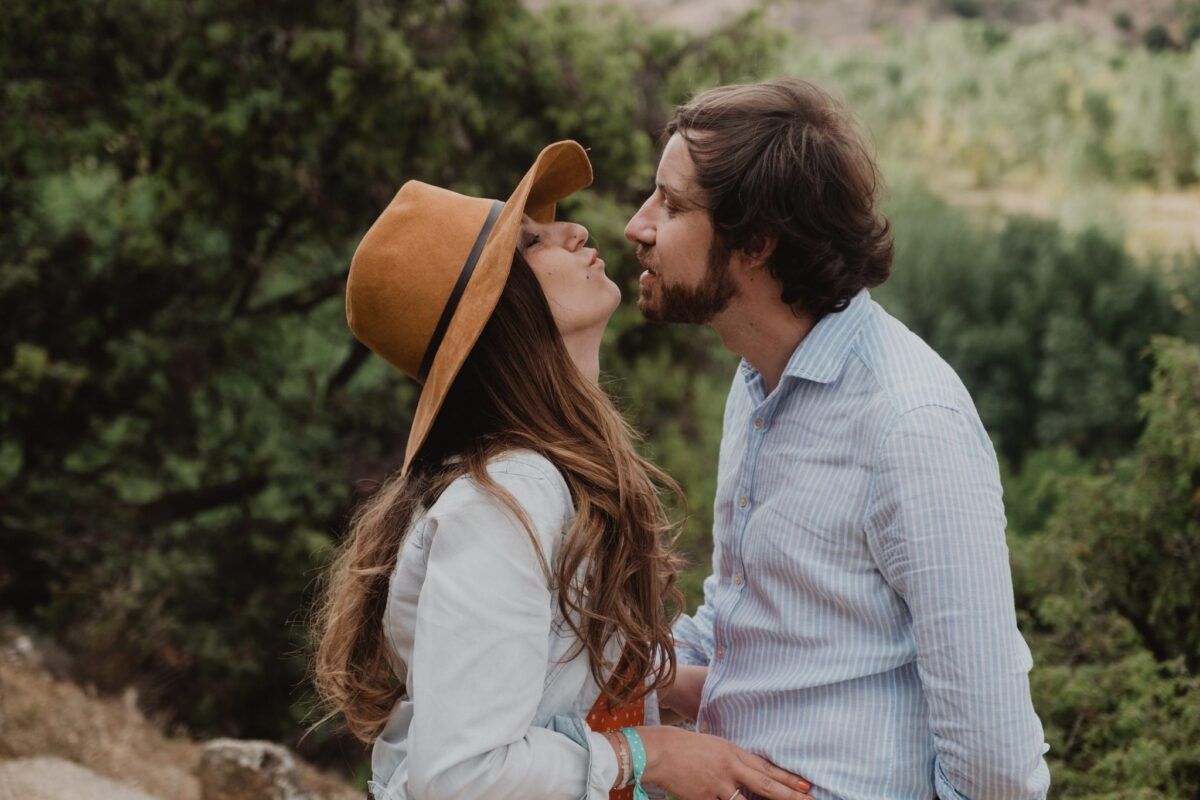 Natalia, con sombrero, y David acercándose para besarse entre la vegetación.