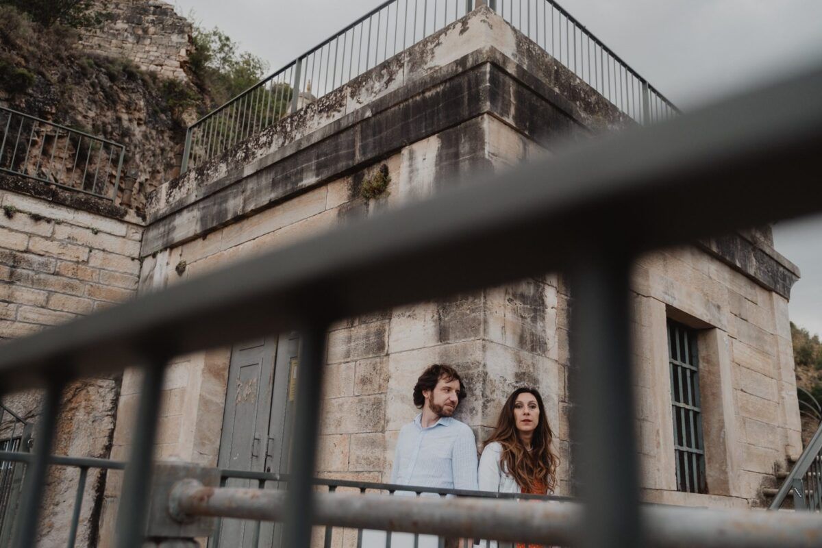 Natalia y David junto al edificio de piedra del Pontón de la Oliva, enmarcados por una barandilla.