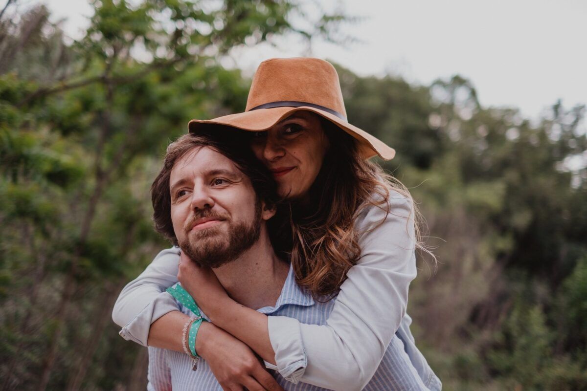 Natalia, con sombrero marrón, abraza a David por los hombros entre los árboles.