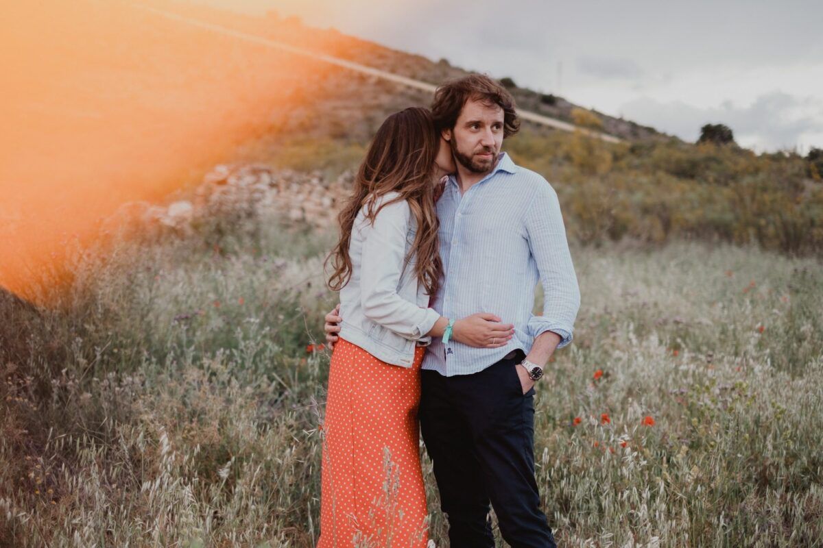Natalia y David abrazados en el campo, con un reflejo anaranjado en primer plano.