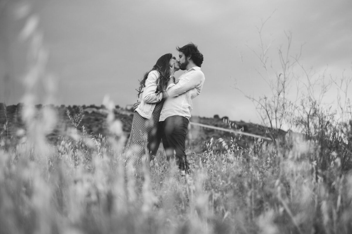 Natalia y David besándose entre la hierba durante su preboda, en blanco y negro.