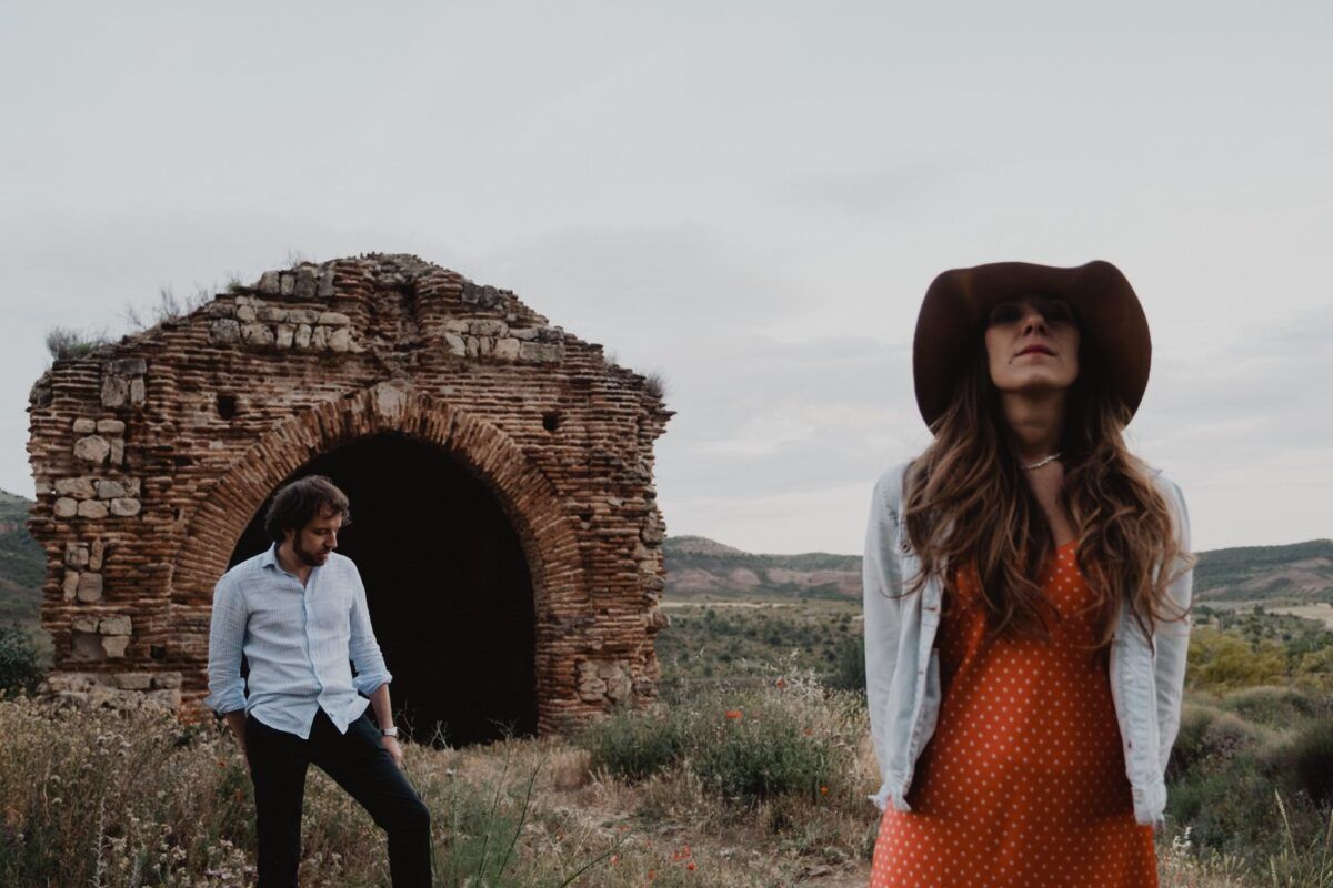 Natalia con sombrero en primer plano y David junto al arco de ladrillo al fondo.