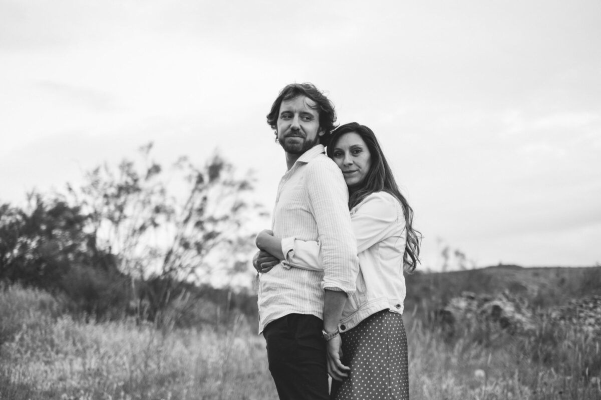 Natalia abraza a David por detrás en el campo durante su preboda en el Pontón de la Oliva, en blanco y negro.